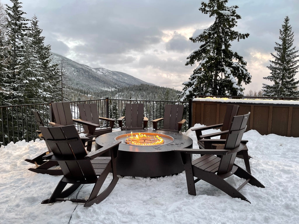 A lit Unity Round Steel Gas Fire Pit 18" High (3 sizes) in an outdoor mountain patio during winter.