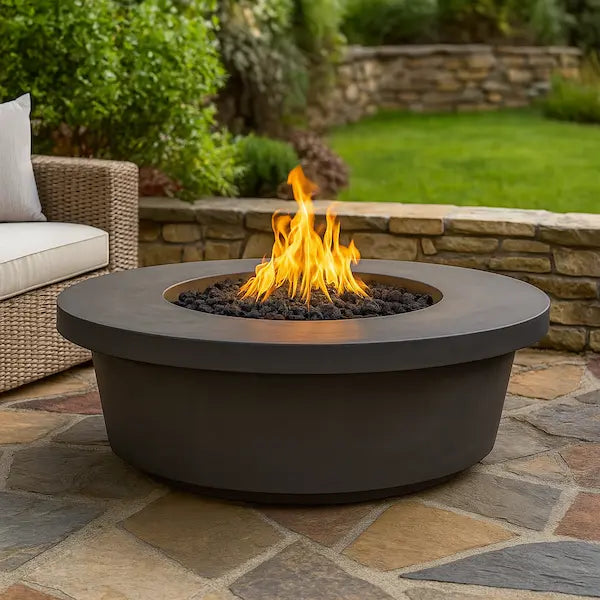 Tempe fire pit table with flames on a stone patio with outdoor furniture and greenery.