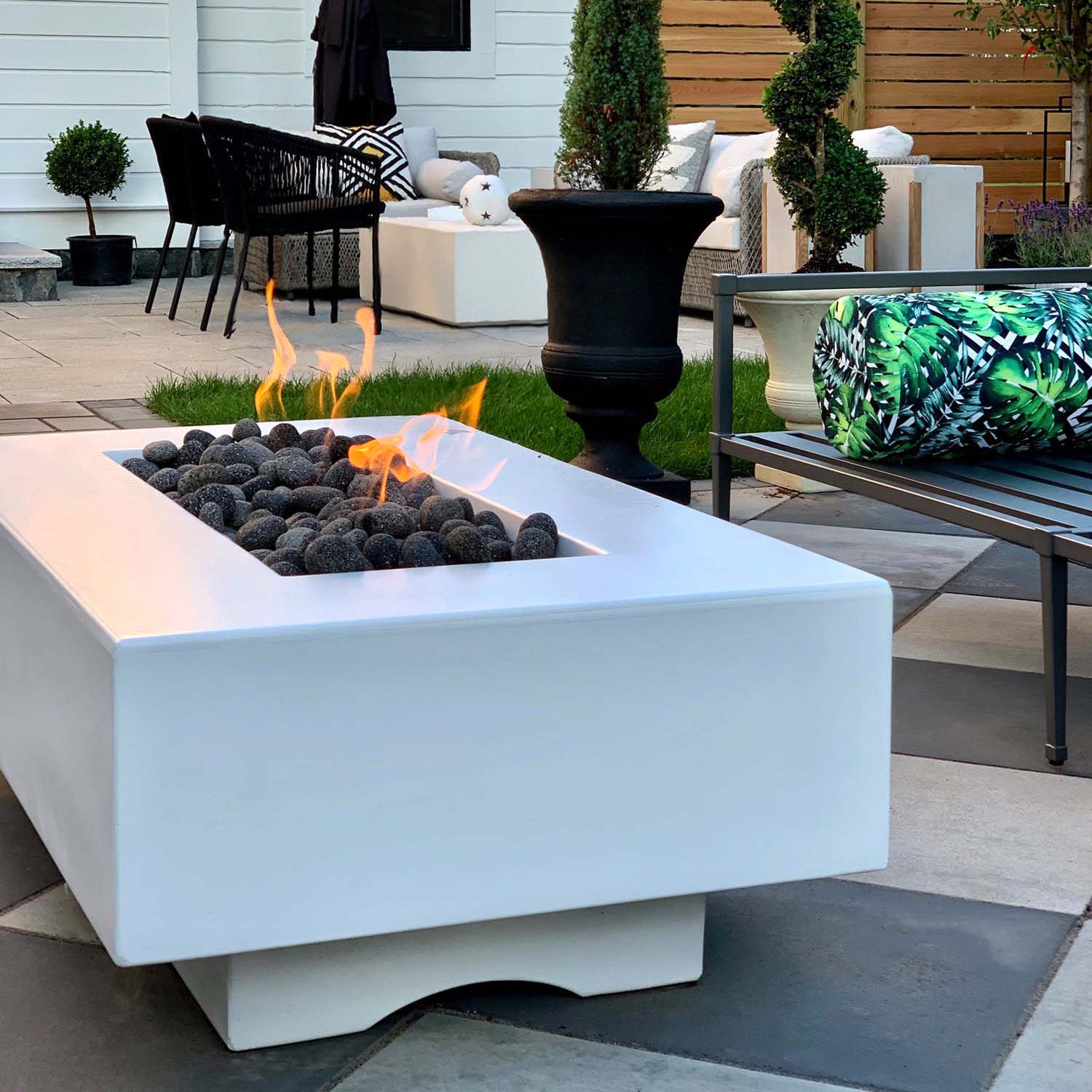 Del Mar Gas fire pit in limestone color variation lit up in a modern backyard.